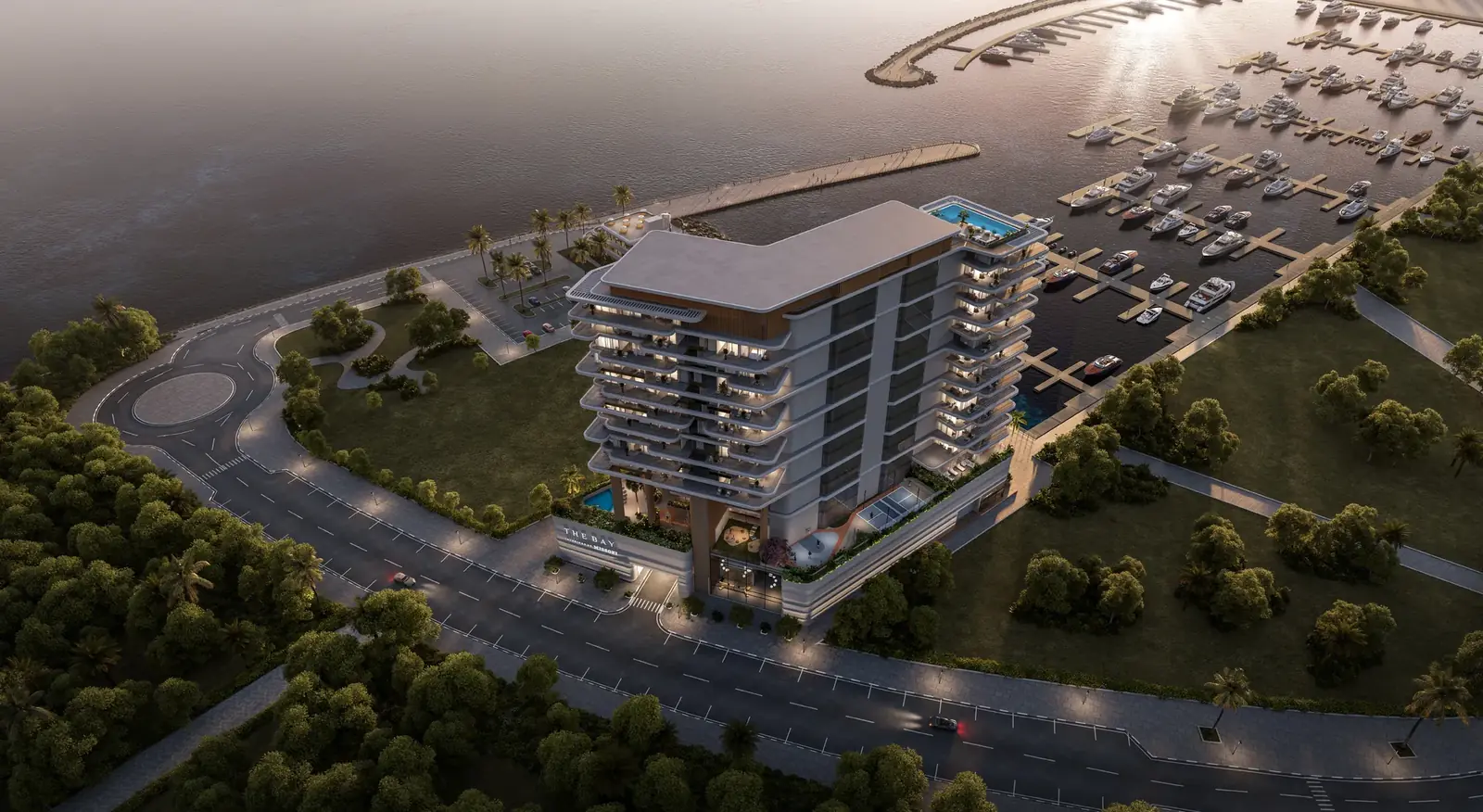 Dusk aerial of The Bay Interiors by Missoni on Dubai Islands, Island A, with lit windows, a rooftop pool, and the yacht marina beside the tower